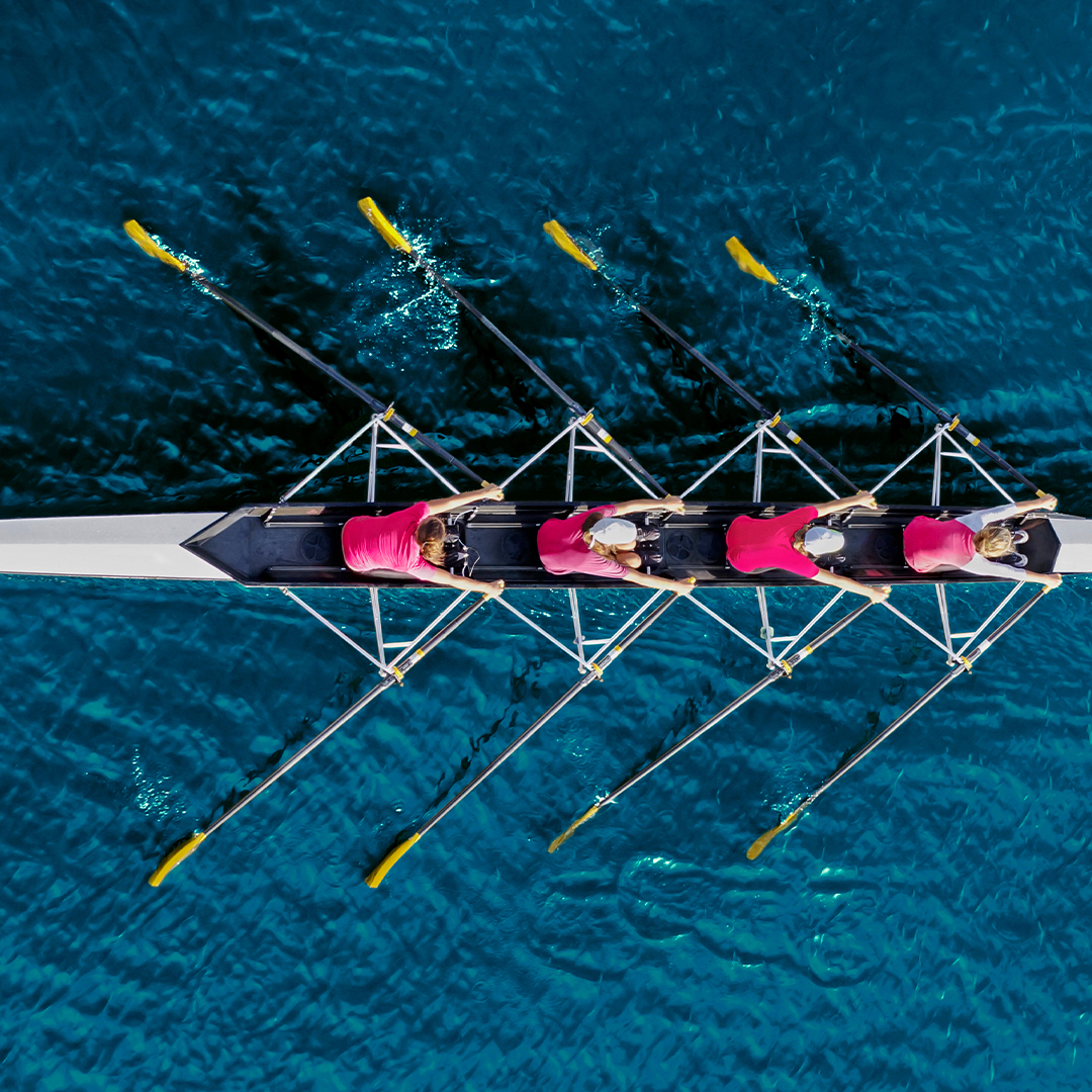 Team of rowers in long rowboat on blue water - Odgers Executive Search Board Headhunters