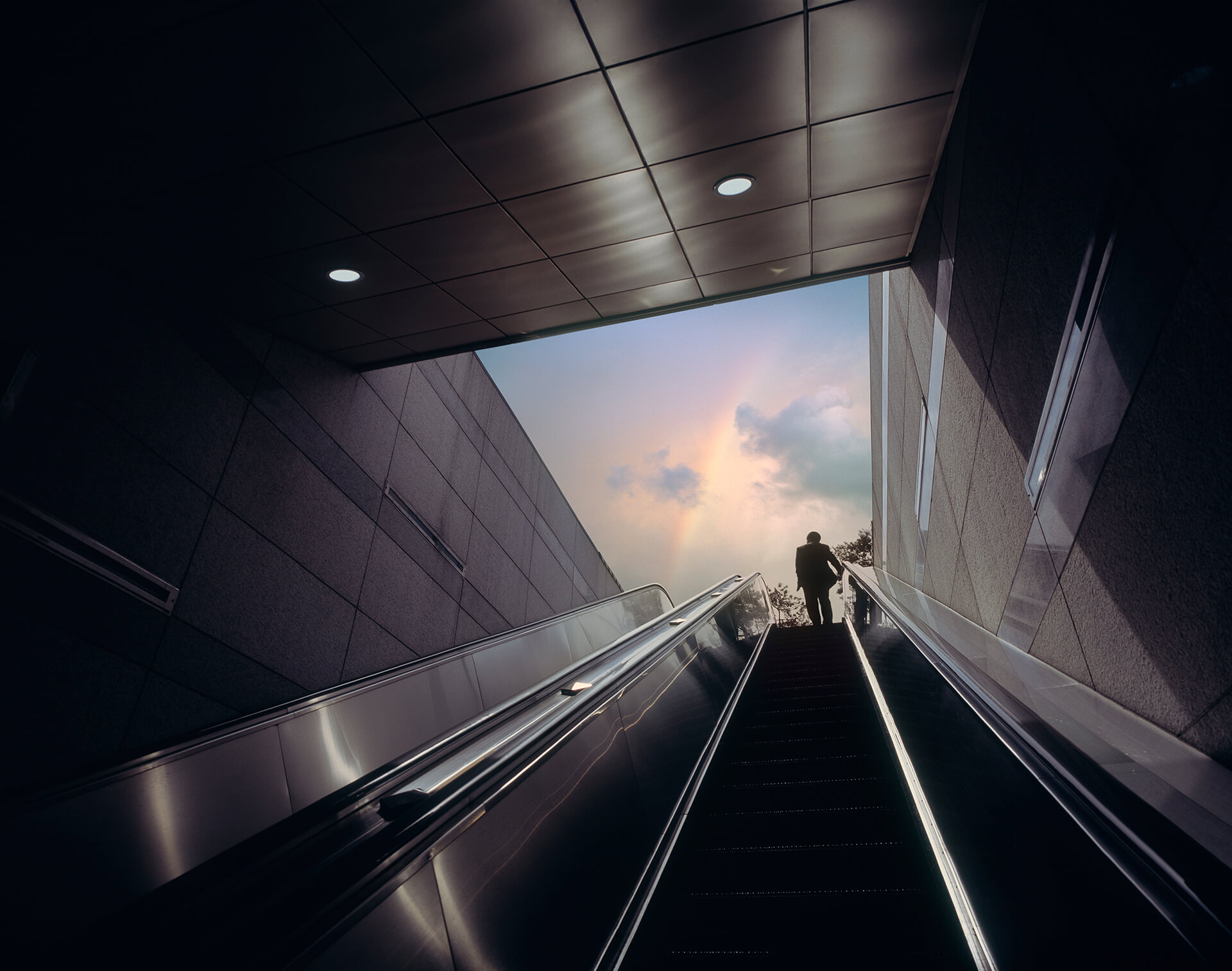odgers berndston man going up escalator with the view of rainbow in the sky