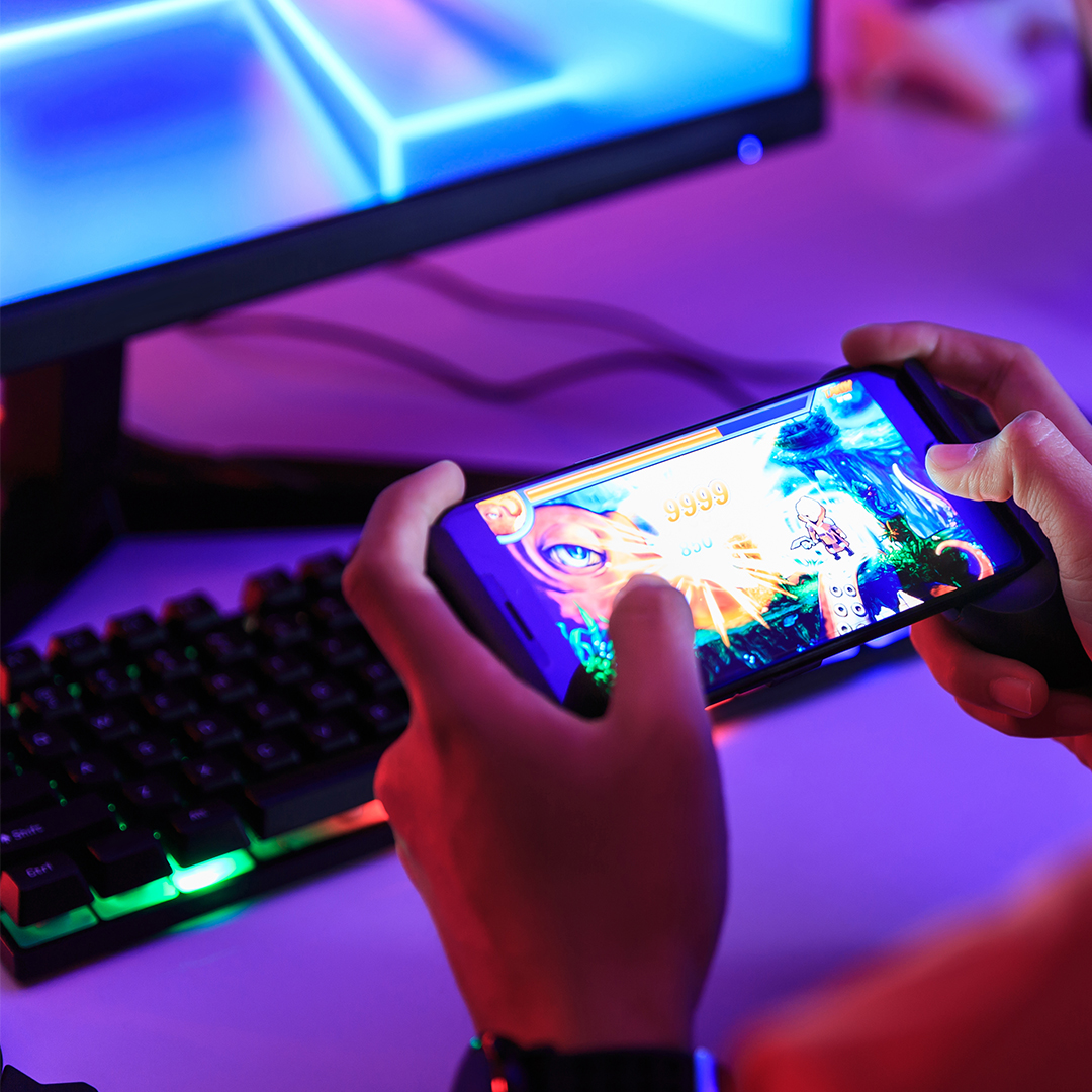 Person playing a game on phone - computer and keyboard in the background, lit by neon lights - Odgers Executive Search Board Headhunters