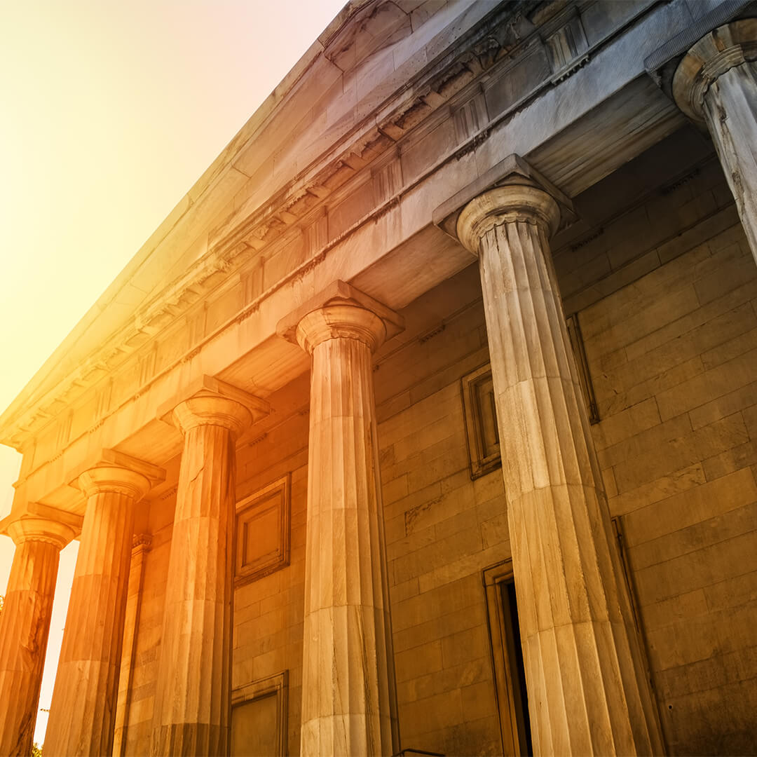 Classic stone building with columns and sun shining from behind it - Odgers Executive Search Board Headhunters