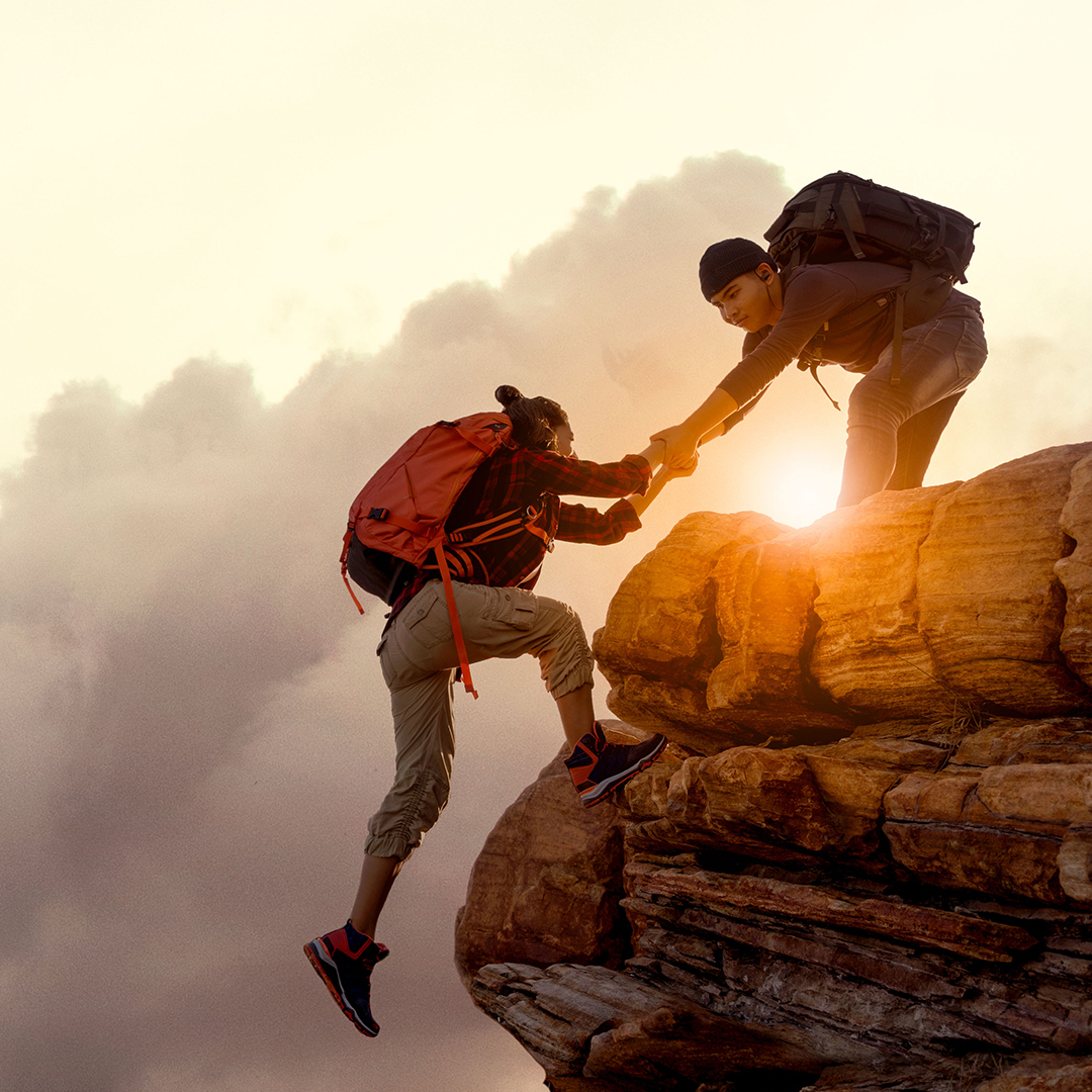 Hiker helping another one up a rock face in the sunshine - Odgers Executive Search Board Headhunters