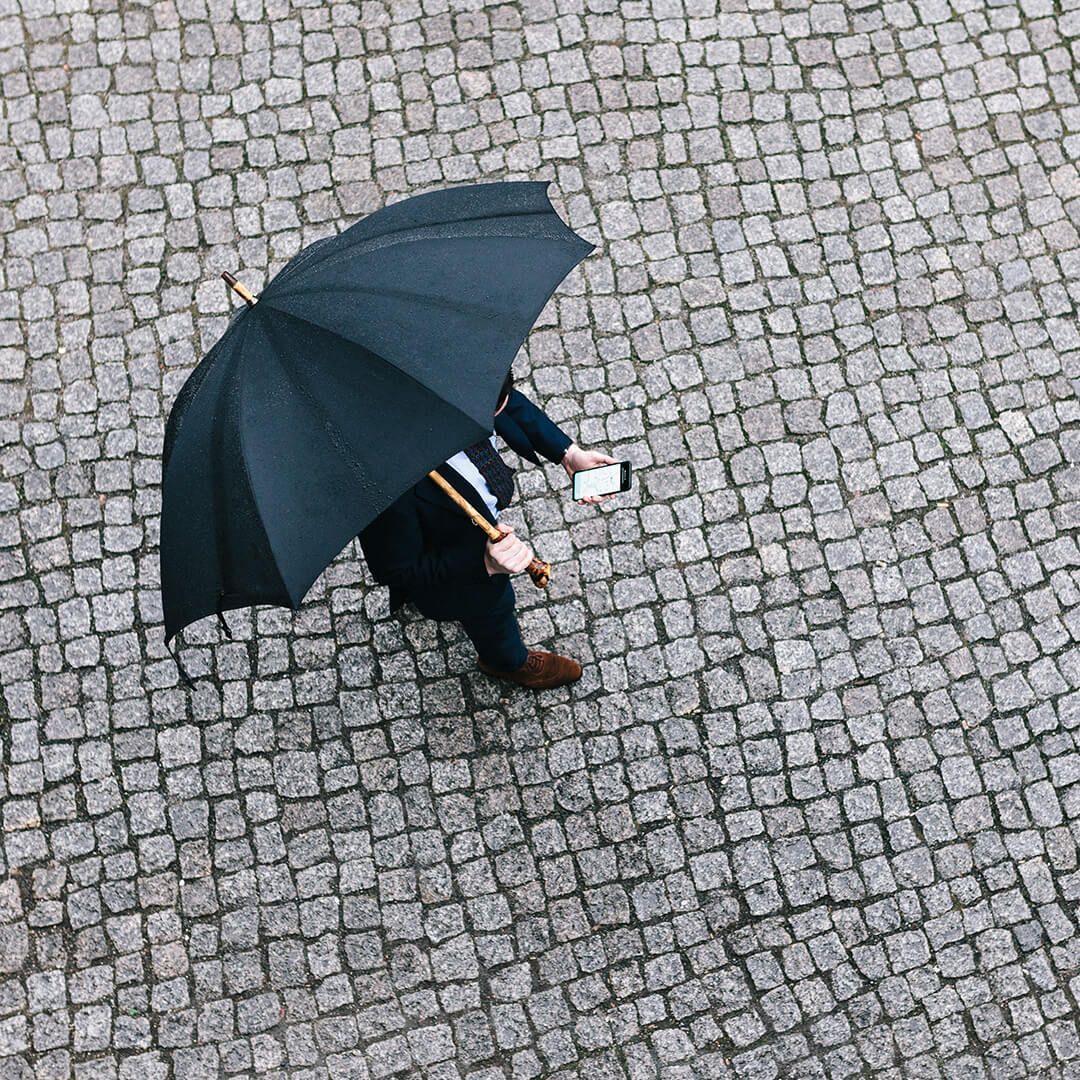 odgers berndtson man with umbrella looking at cell phone on cobbles